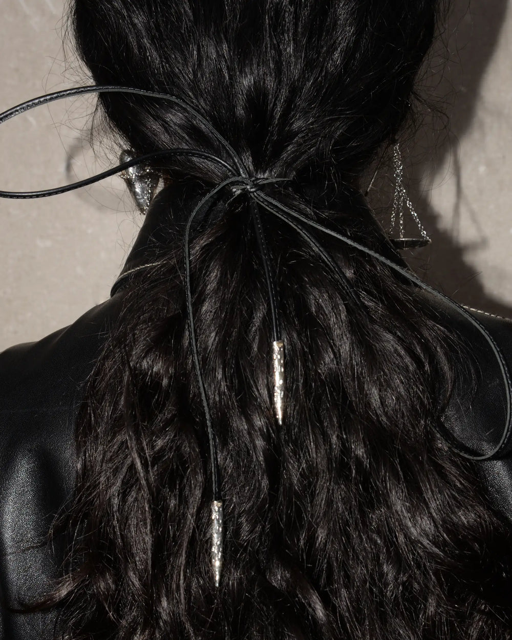 Black leather ribbon with silver metal tips, tied around a low ponytail with a bow for a stylish and polished look. That can be customized with one of our charms for a personalized touch, offering versatile styling options.