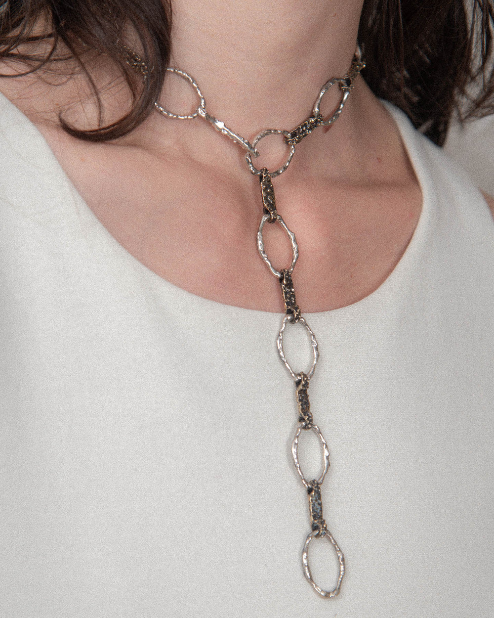 A woman wears a long, elegant handmade chain necklace from Naples, Italy, featuring a molten, textured finish. Fitted snugly at the neck, it exudes sexy chic and timeless sophistication.