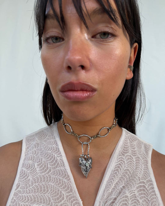 Silver heart-shaped pendant adorned with a vibrant peridot stone, elegantly hanging on a delicate chain necklace, perfect for adding a touch of gemstone elegance to any outfit.