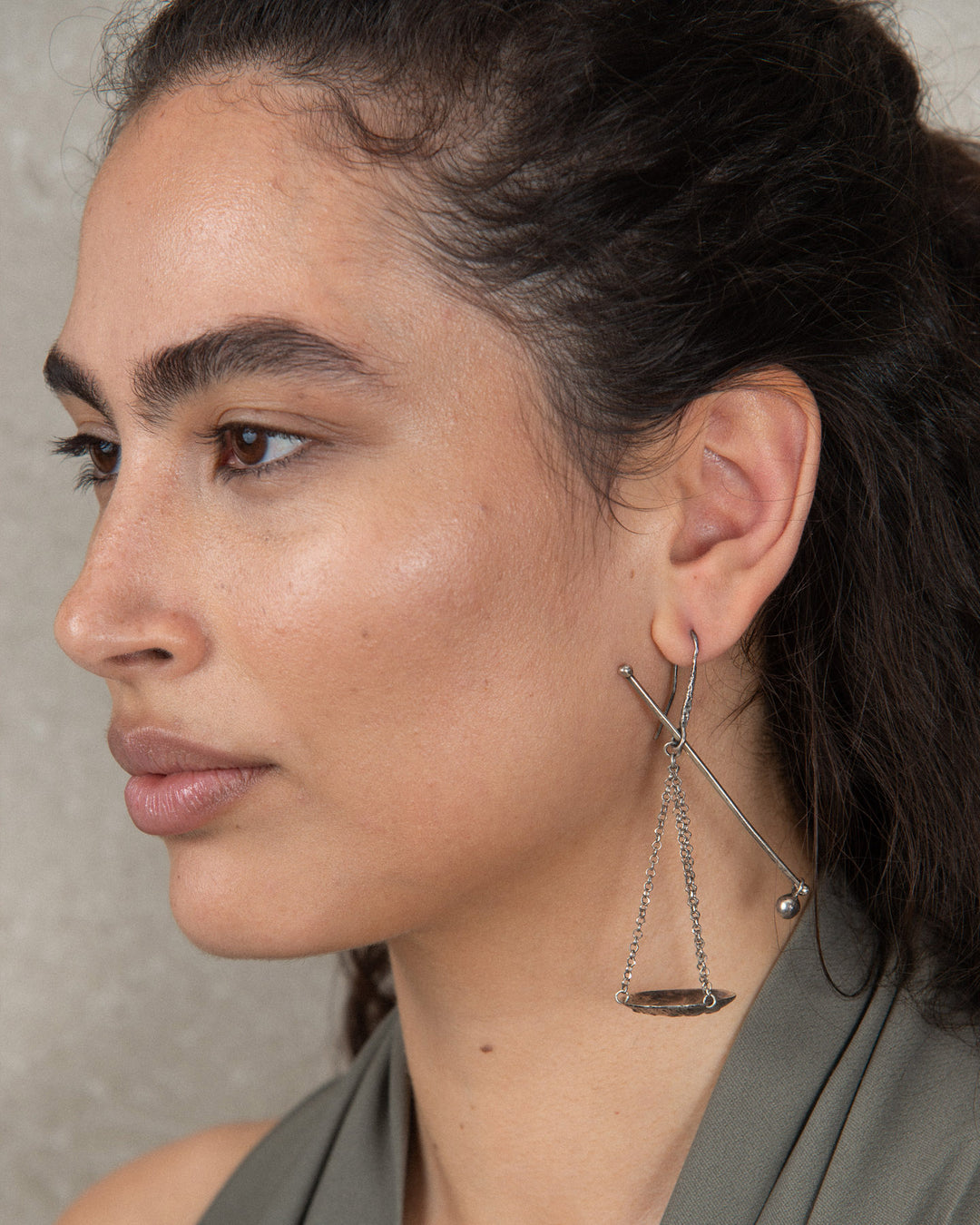 A single silver dangling earring featuring a scale or balance weight. Worn by a sophisticated woman.