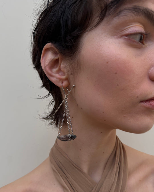 Close-up of a person wearing a delicate silver earring against a neutral background