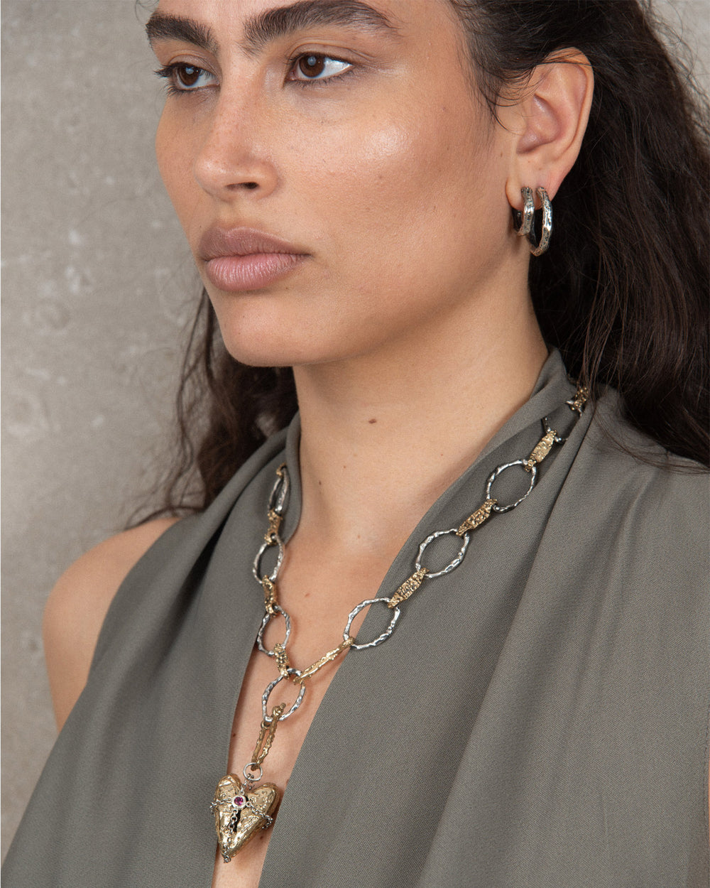 Bronze talisman with textured finish, featuring a locket-style opening and wrapped in a silver chain forming a cross pattern with a central gemstone, adorning a stylish necklace. Elegant jewelry piece with intricate design and mixed metals.