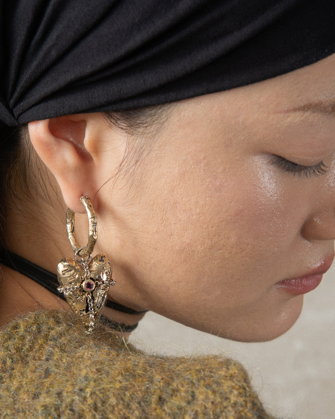 Bronze heart-shaped charm with textured finish, hanging from a hoop earring. The earring features a sleek, polished design that complements the pendant, creating a stylish and cohesive jewelry look.
