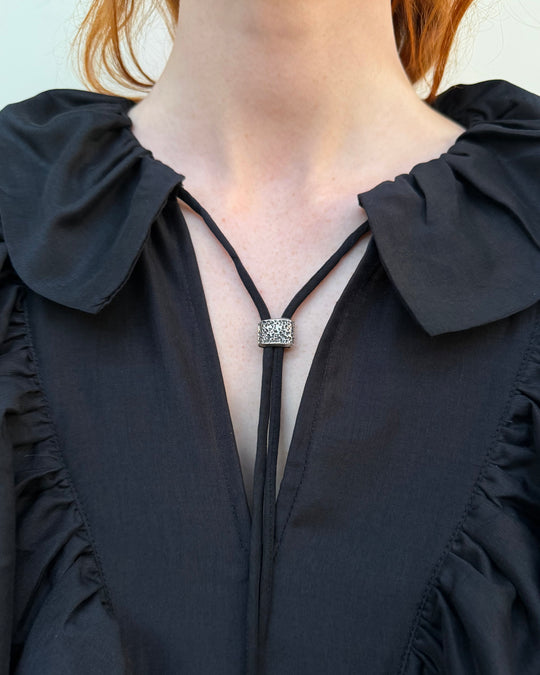 Close-up of a woman wearing a black blouse with a necklace featuring a square pendant.