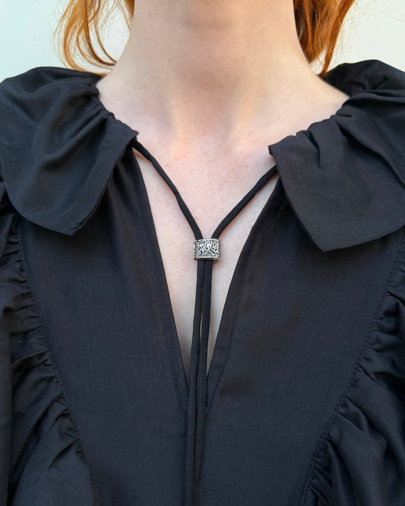 Close-up of a woman wearing a black blouse with a necklace featuring a square pendant.