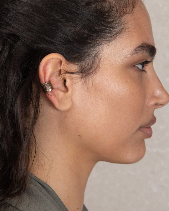 Side view of a minimalist yet bold golden earring with hammered detailing