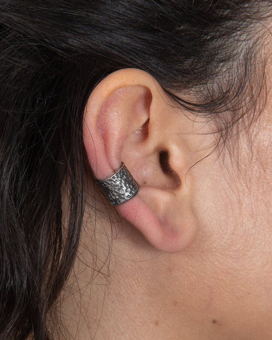 A close-up of a textured silver ear cuff worn on the ear.