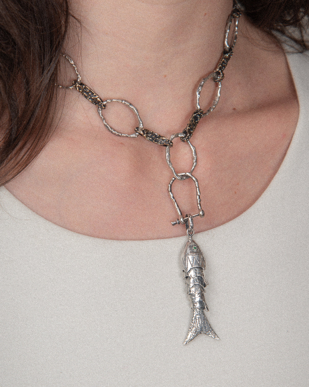 A woman showcasing a modern, textured layered jewelry look with three standout pieces: a bold chain necklace, a charm, and a shackle clasp. The look combines edgy and refined elements, starting with the chain as the base, adding the charm for elegance, and connecting them with the shackle clasp for a polished finish.