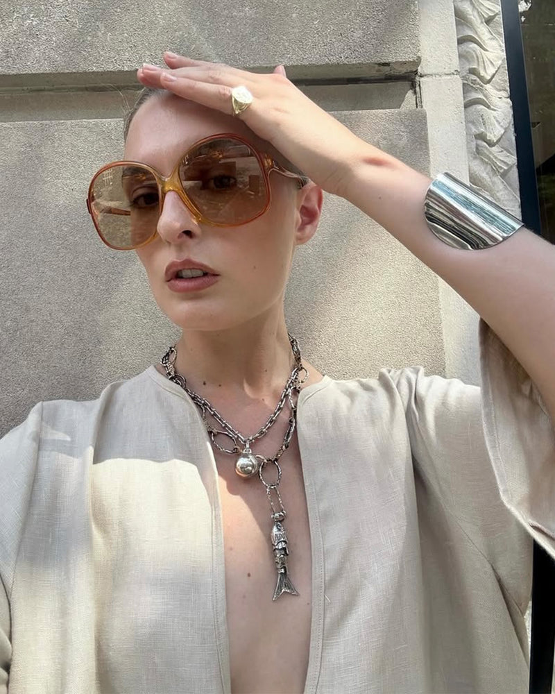 Christie Tyler styling the chain statement necklace with large sunglasses and a beige linen outfit 
