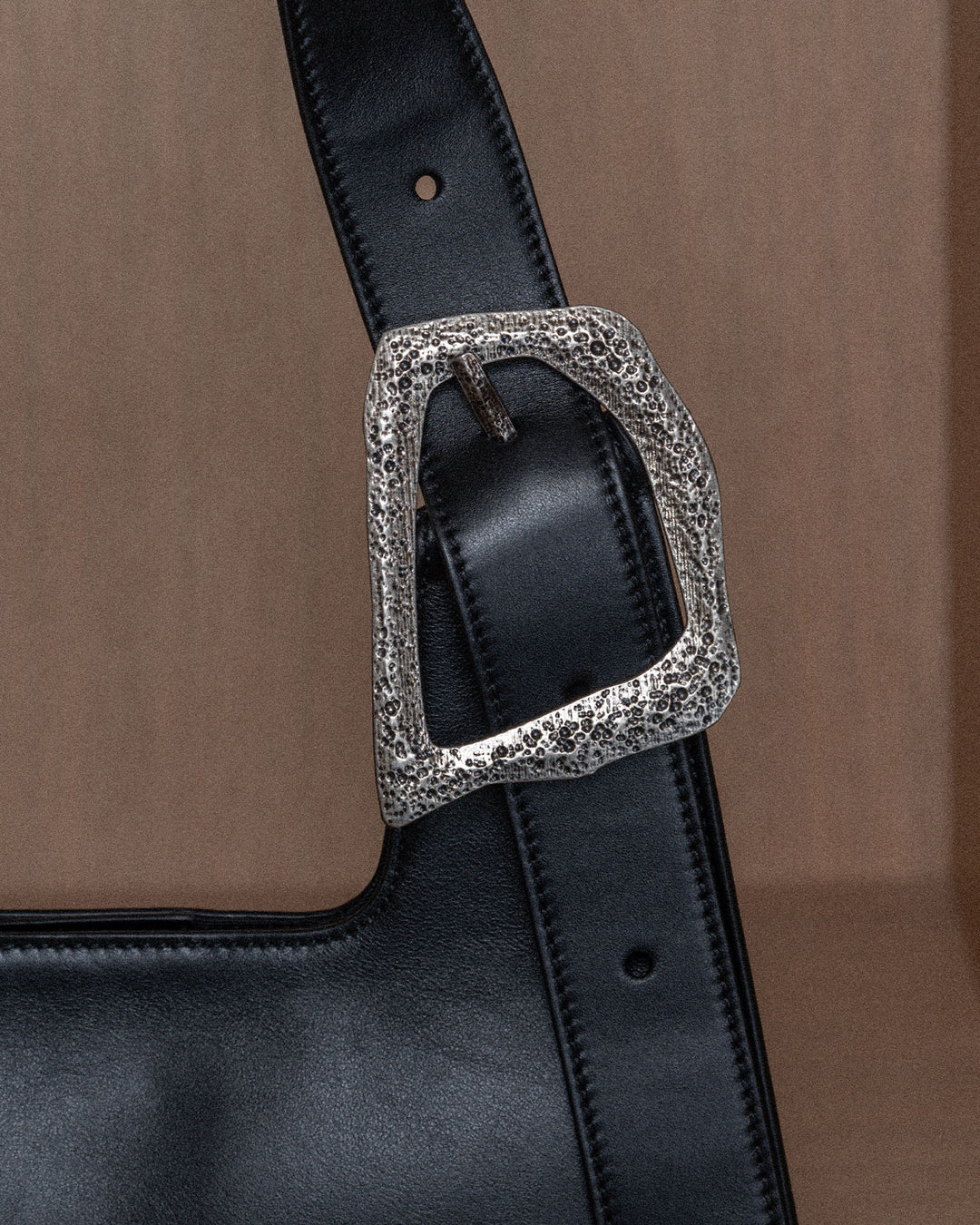 Close-up of a luxurious silver buckle on a black upcycled leather bag.