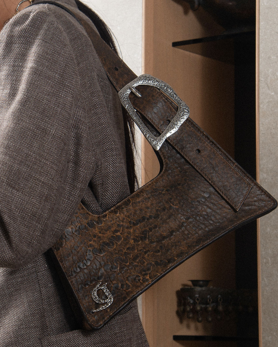 A close-up of a handbag with a crocodile-printed leather texture, featuring a prominent buckle, worn by a woman.