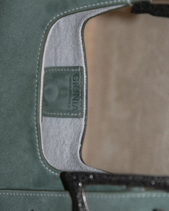 A highly detailed close-up of the suede handbag, showcasing the white canvas lining matching the topstitches and featuring a subtle logo on the magnetic closure. The scene emphasizes the craftsmanship and luxurious details of the accessory, set against a clean, elegant background.