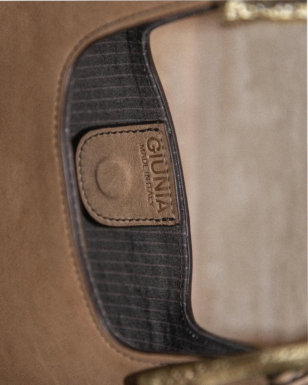 A close-up shot of a vintage tobacco-colored handbag featuring a cotton pinstriped lining with a logo and a magnet closure. The textured, aged leather showcases its timeless charm.