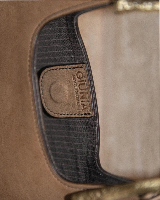 A close-up shot of a vintage tobacco-colored handbag featuring a cotton pinstriped lining with a logo and a magnet closure. The textured, aged leather showcases its timeless charm.