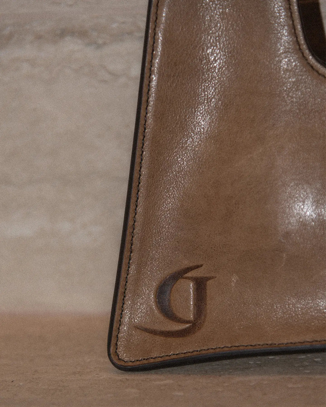 A close-up of a vintage tobacco-colored leather handbag featuring GIUNIA logo in the corner and showcasing a textured, aged leather surface.