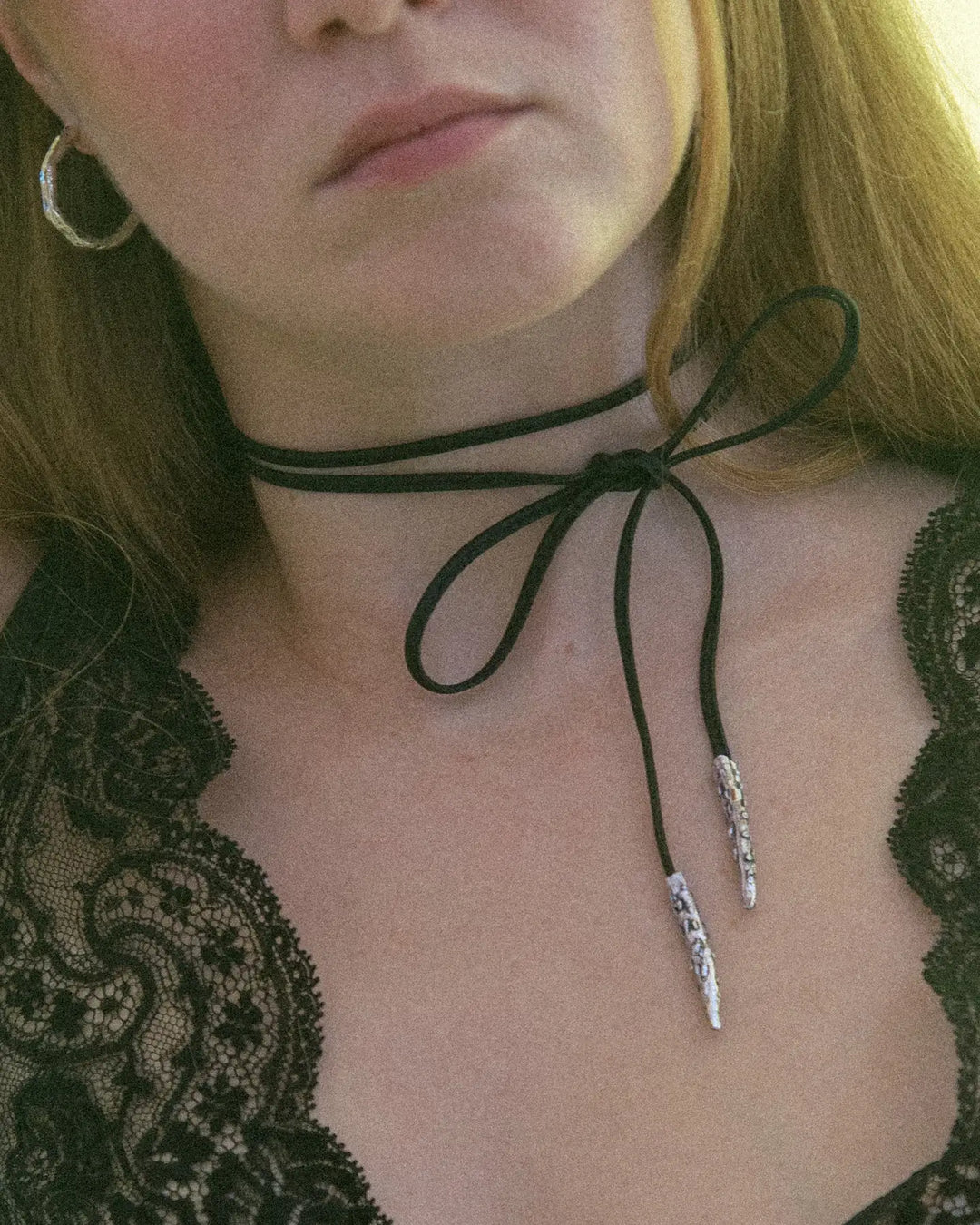 Black leather ribbon with silver metal tips, styled around the neck with a bow for a cute and charming look.