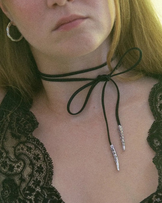 Black leather ribbon with silver metal tips, styled around the neck with a bow for a cute and charming look.