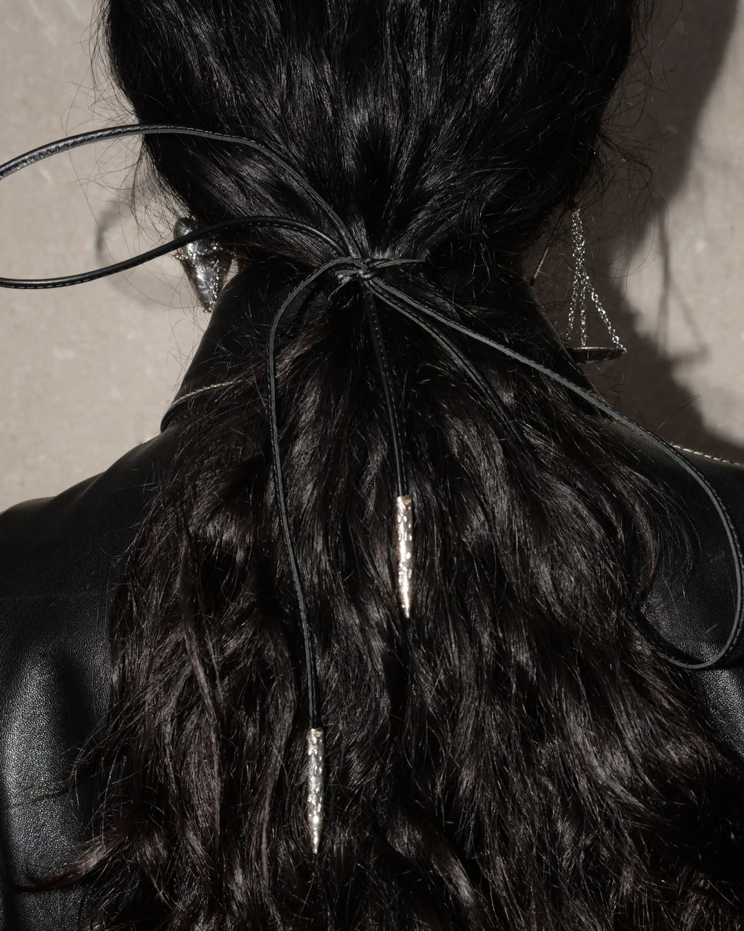 Black leather ribbon with silver metal tips, tied around a low ponytail with a bow for a stylish and polished look. That can be customized with one of our charms for a personalized touch, offering versatile styling options.
