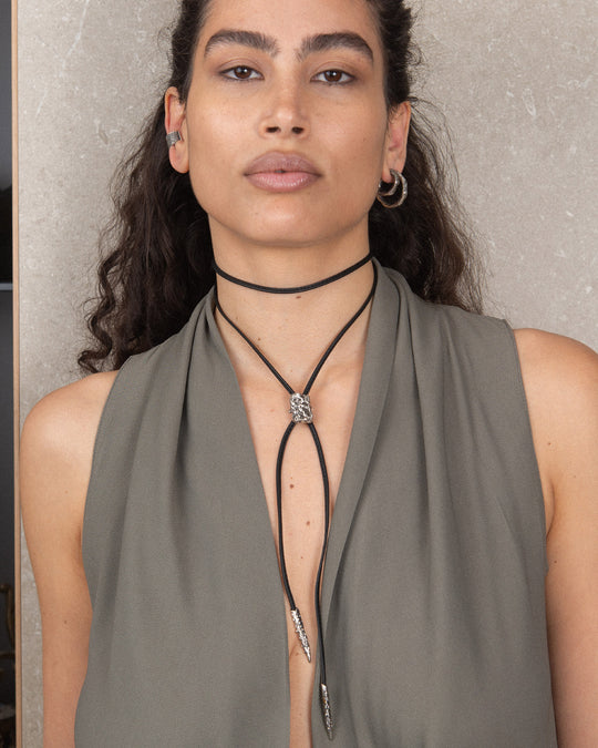A model wearing the black leather ribbon as a choker, adorned with a textured unisex silver charm that is sleek and sophisticated. The minimalist design offers a modern and elegant look, perfect for versatile styling and customization.