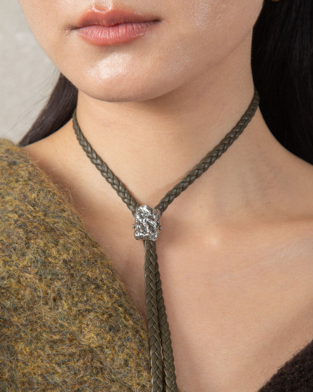 Braided leather choker with textured metal bolo tie-style charm, unisex design, black leather with silver-tone metal accents