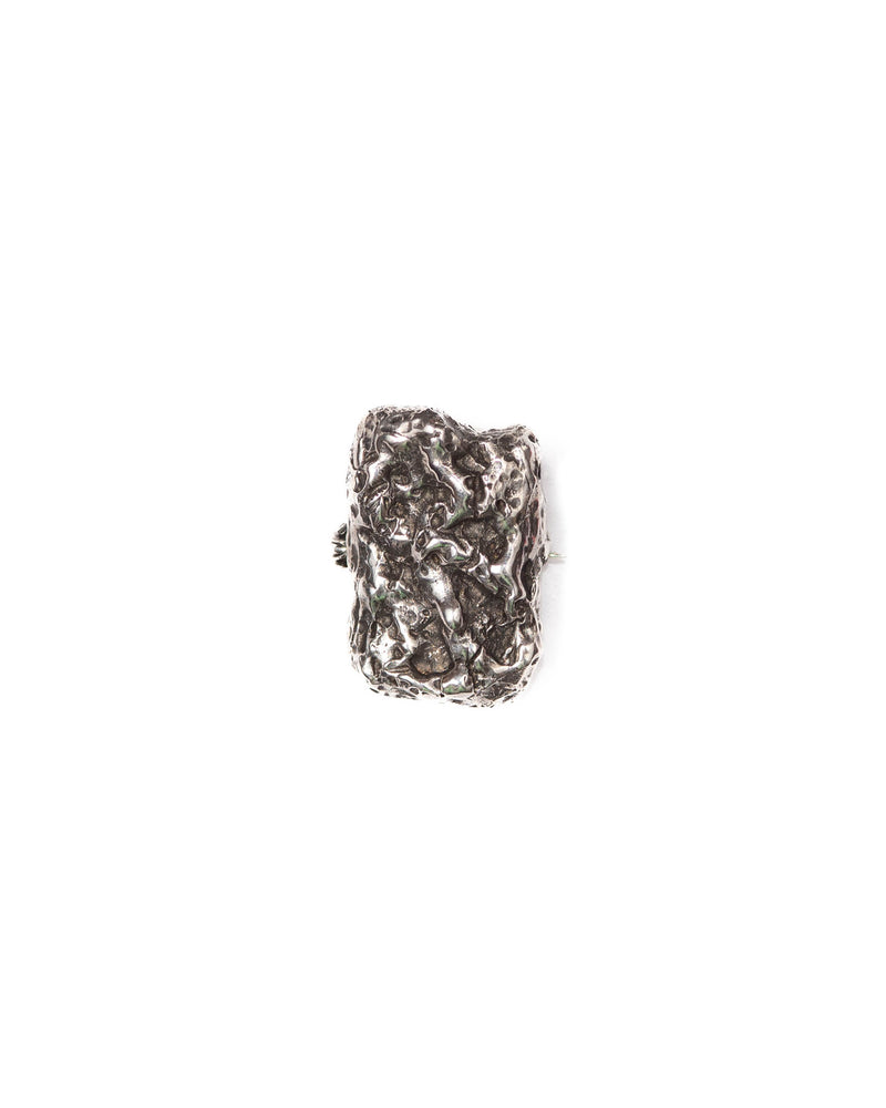 A silver charm/brooch with a textured, moon-like surface