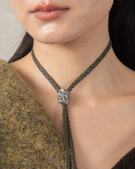 A silver moon-shaped charm with a textured surface, featuring craters and ridges, set on an olive green choker