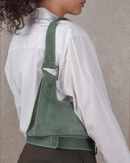 The view is from the back, showing a woman wearing a sage suede belt with a debossed logo and a matching handbag.