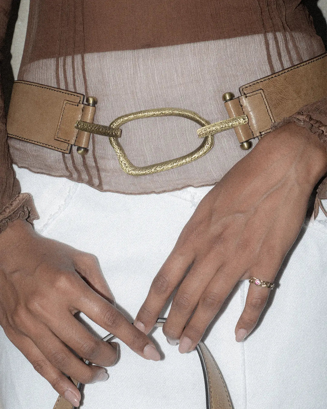 Close-up of a woman wearing a brown belt with a vintage finish and a bold, hammered eye-shaped metal statement piece.