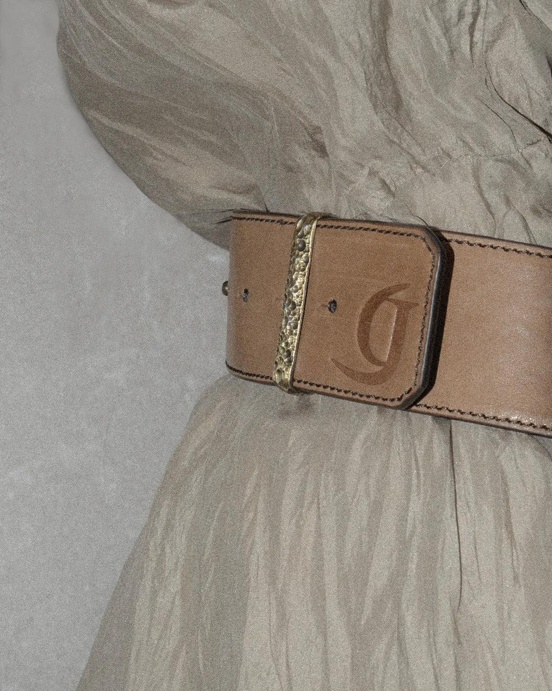 Close-up of a brown belt featuring a debossed logo and a hammered bronze metal belt loop.