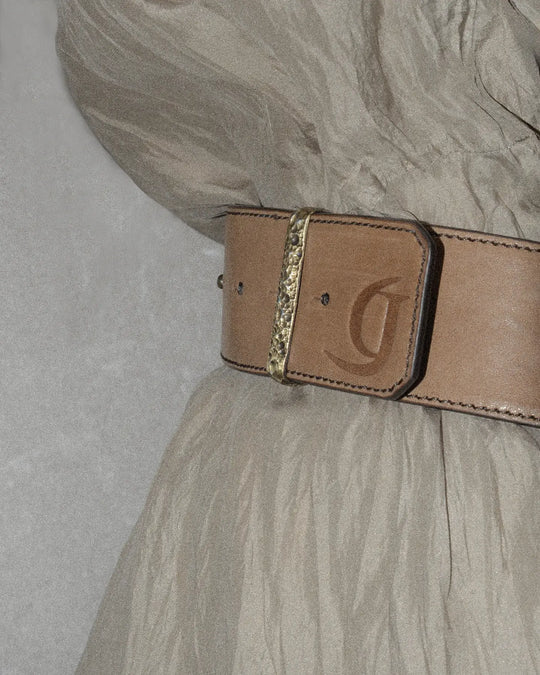 Close-up of a brown belt featuring a debossed logo and a hammered bronze metal belt loop.