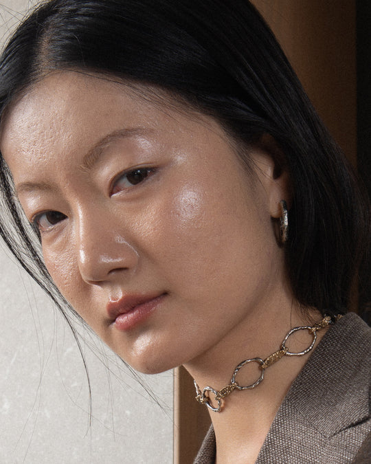 A woman wears a sophisticated handmade chain necklace from Naples, Italy, featuring a molten, textured finish crafted from a stunning combination of silver and bronze, adding a unique twist. Designed to be worn as a chic choker, it exudes timeless elegance and sexy allure.