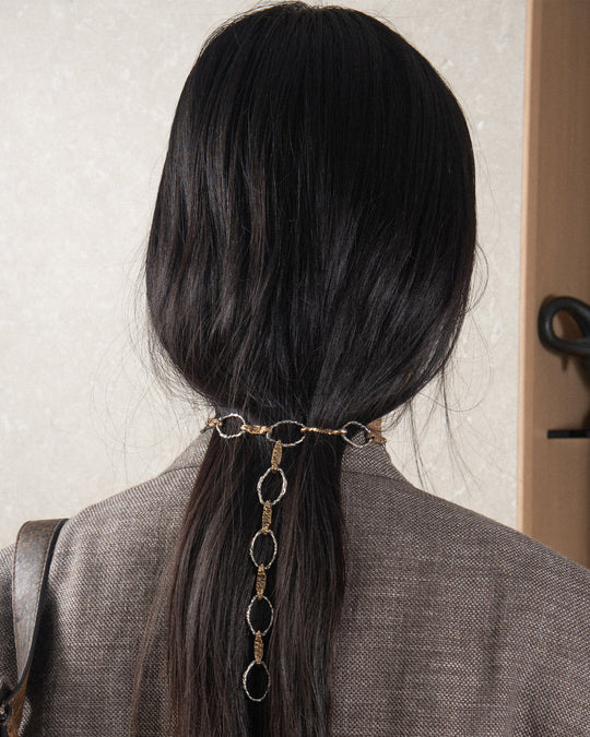 A woman showcases a handmade chain necklace from Naples, Italy, featuring a striking blend of silver and bronze with a molten, textured finish that adds a distinctive twist. Designed as a chic choker, the chain gracefully drapes around her neck, with its intricate details visible on the back, radiating timeless elegance and sensual allure.