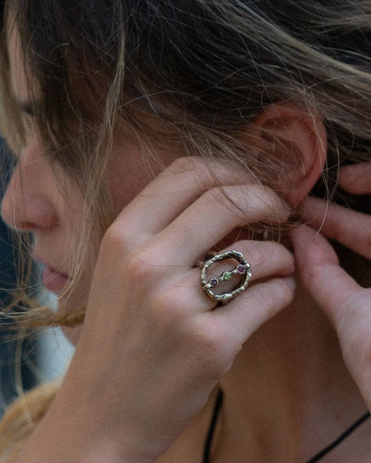 woman showing an elegant golden ring with natural pink and green gemstones