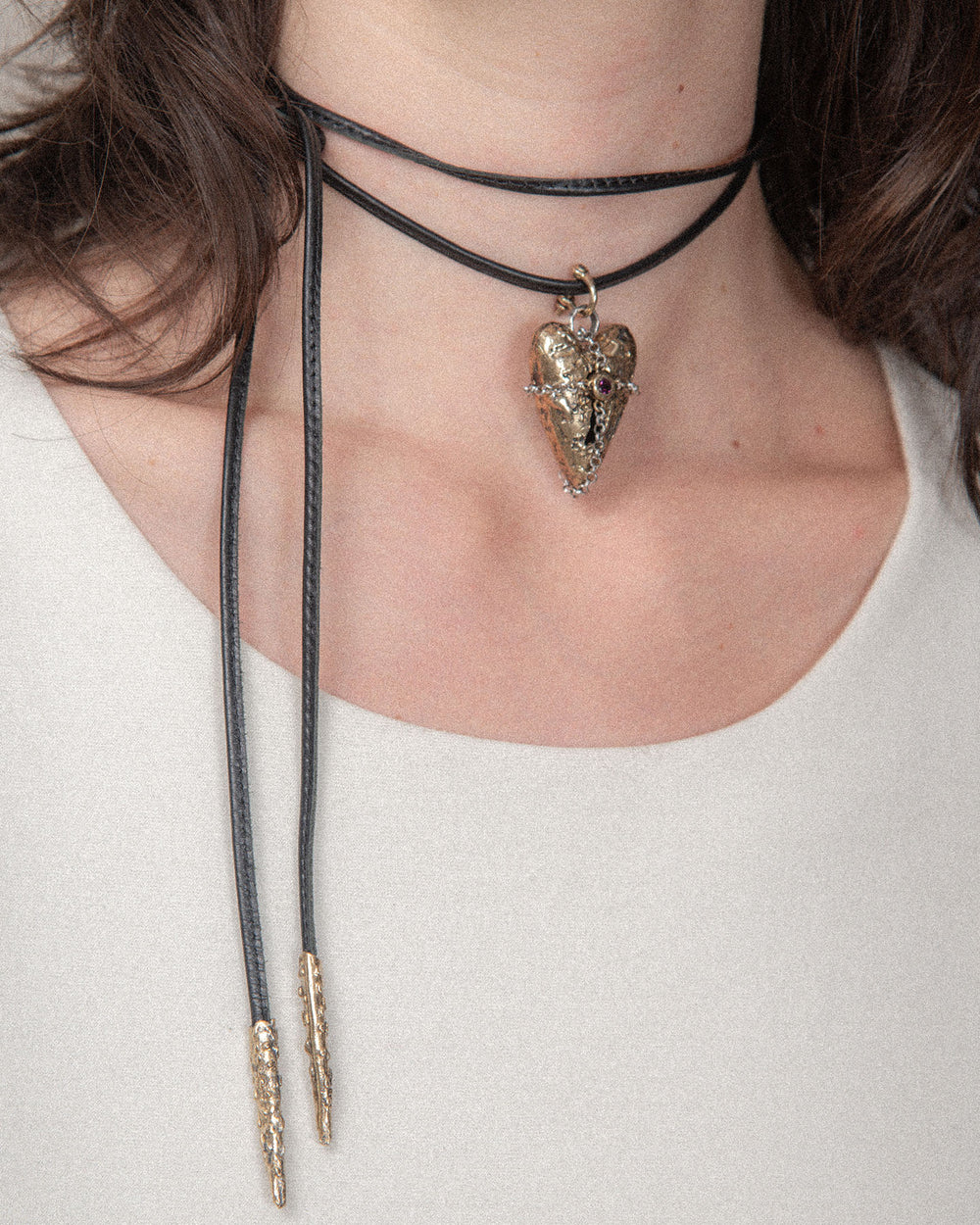 Close-up of a woman showcasing versatile layered jewelry, highlighting her unique and customizable style with a leather choker, shackle clasp, and a heart-shaped charm.