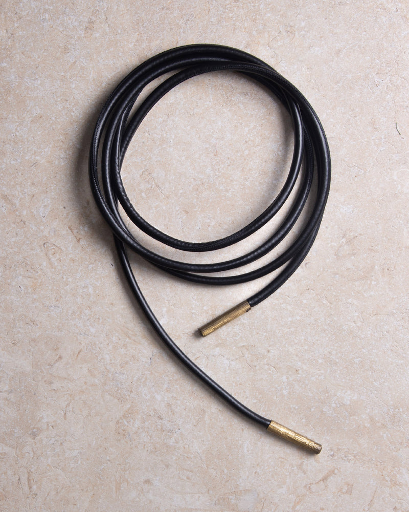 A still picture of a high-quality black leather belt shaped into a circle, with bronze details, placed on a clean background. The focus is on the sleek, minimalist design and smooth texture of the leather, highlighting craftsmanship and the warm, elegant glow of the bronze elements