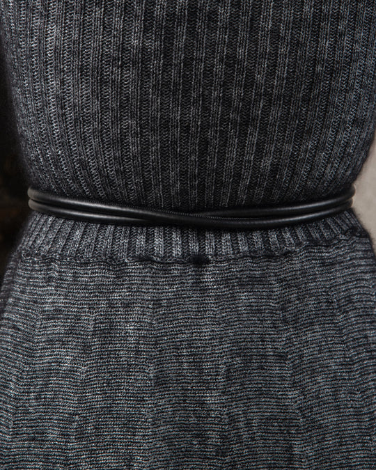 Close-up of the back side of a sleek, minimalist tubular belt in high-quality black leather. The design is streamlined and refined, emphasizing craftsmanship and elegance, showcasing smooth texture and precise craft