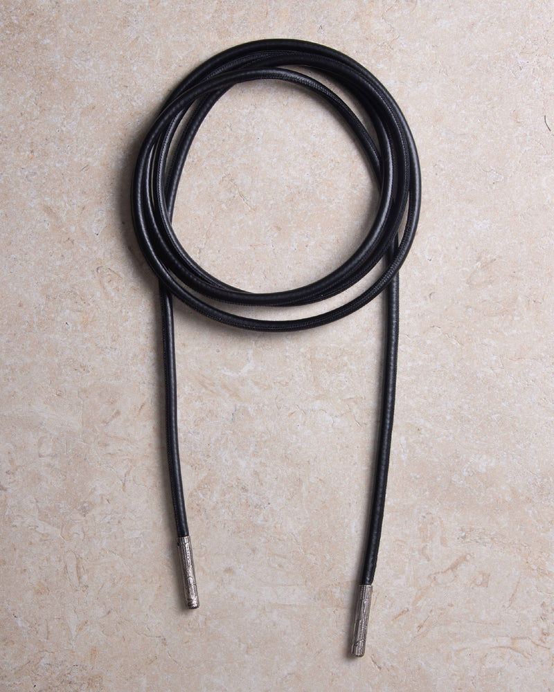 A still picture of a high-quality black leather belt wrapped into a circle, placed on a neutral background. The focus is on the sleek, minimalist design and smooth texture of the leather, highlighting craftsmanship and elegance