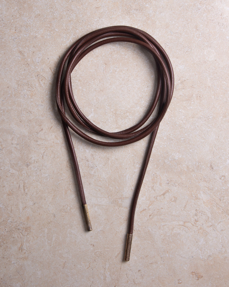 Still shot of a high-quality upcycled leather tubular belt with textured bronze metal details, styled against a marble background