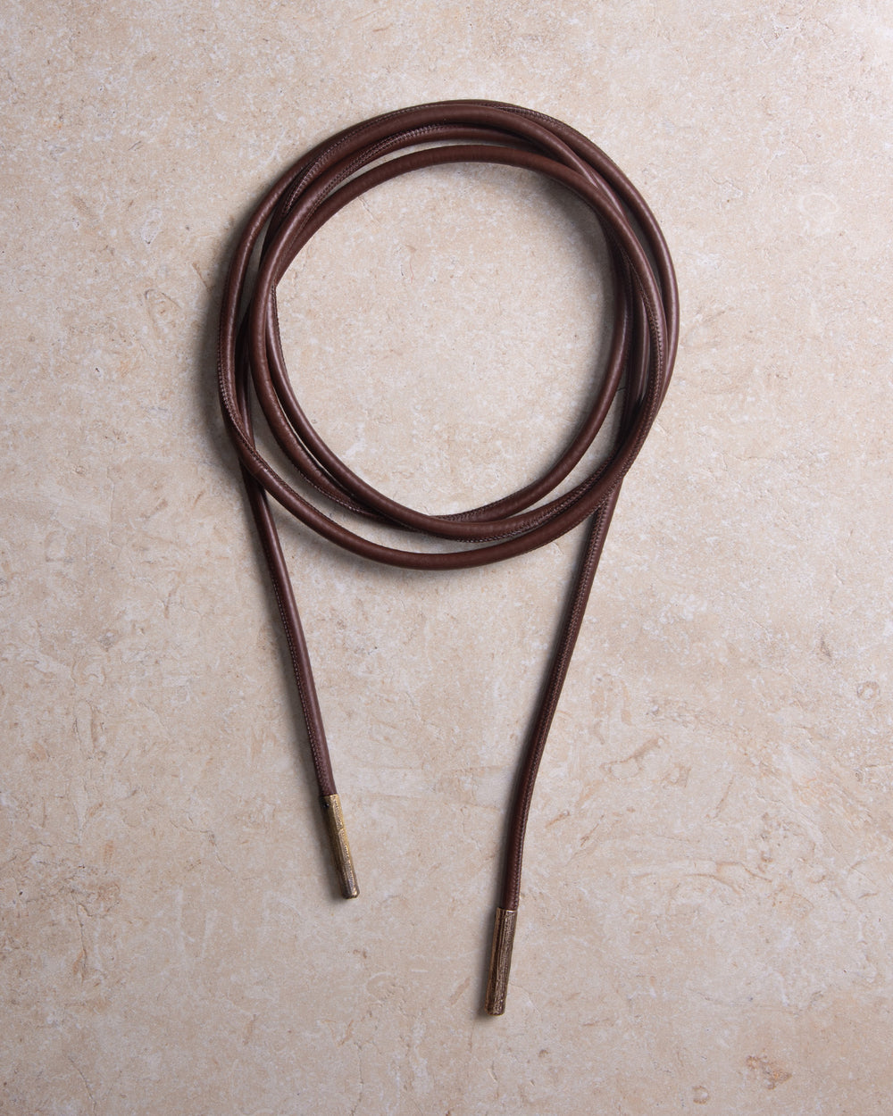Still shot of a high-quality upcycled leather tubular belt with textured bronze metal details, styled against a marble background