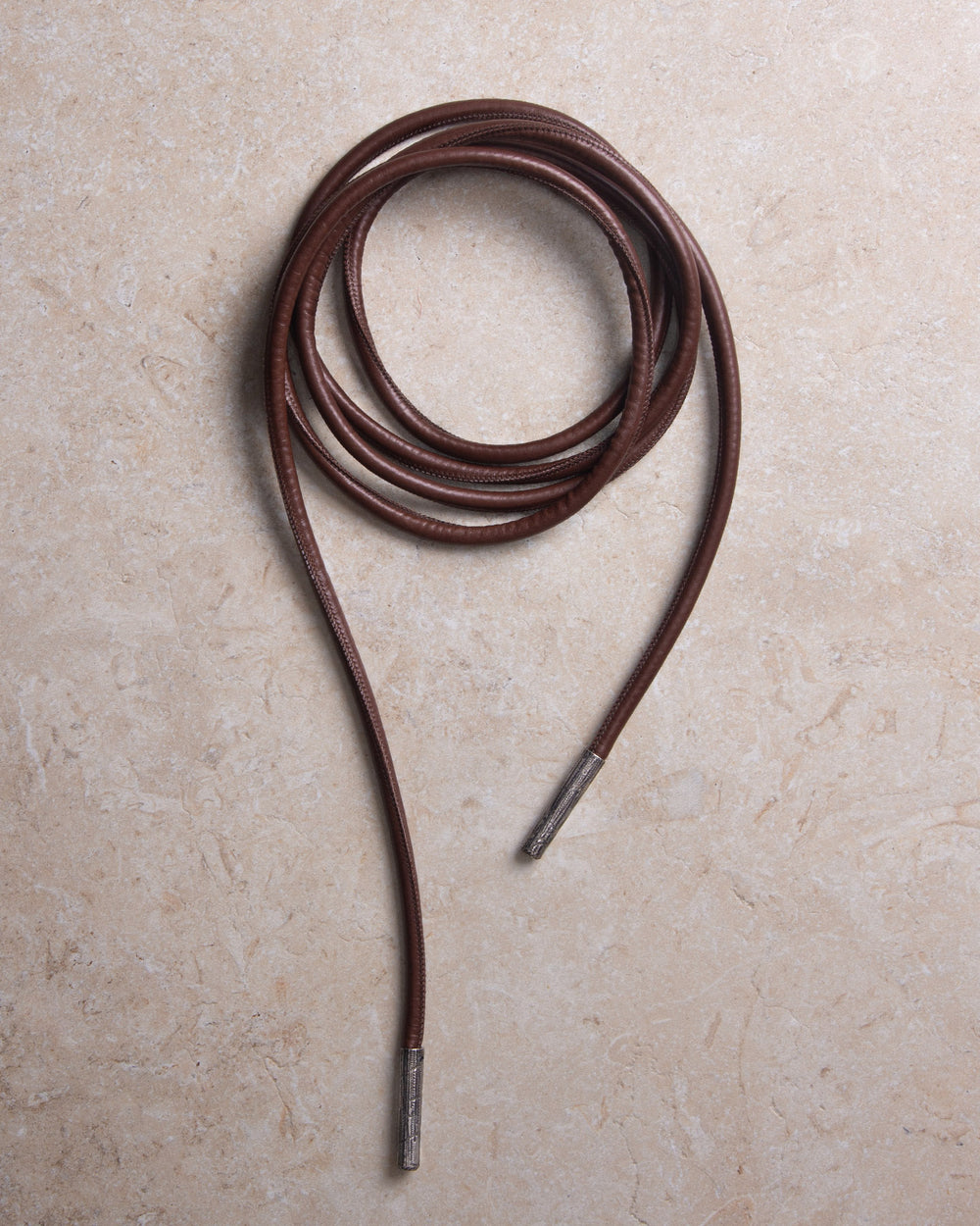 Still image of a tubular rope belt made from high-quality upcycled leather and texturel metal details, styled against a sleek marble background