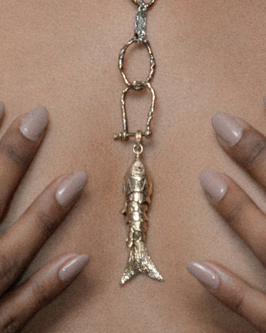 A fish charm hooked onto a chain with a silver horseshoe-shaped clasp, creating a layered, customizable look.