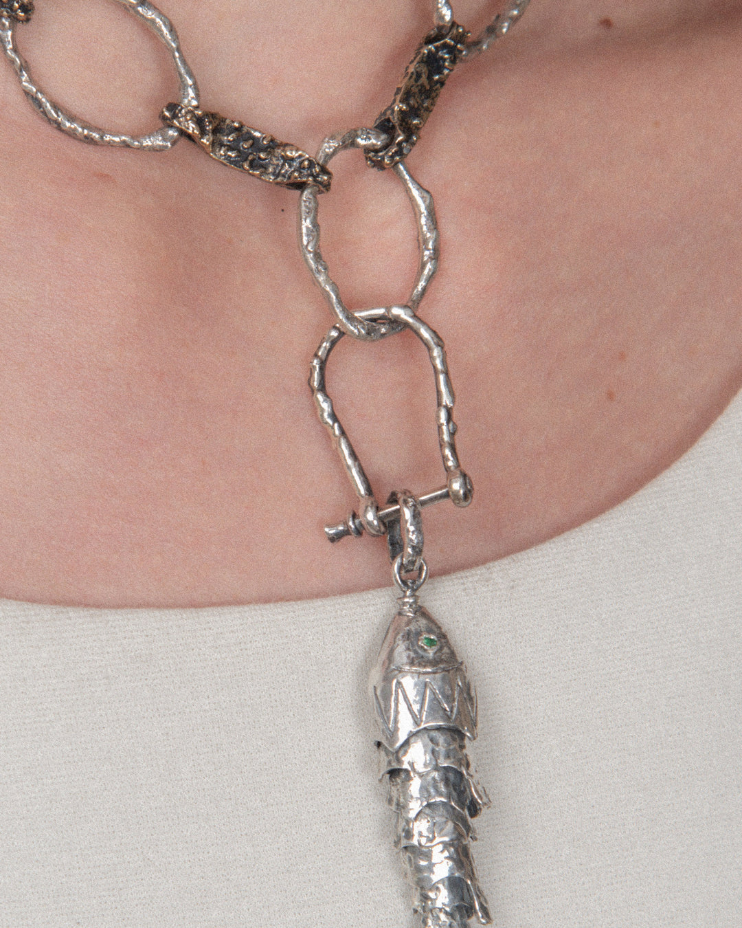 A pendant attached to a chain using a silver horseshoe-shaped clasp, allowing for a layered, customizable look.