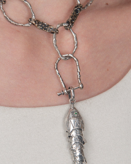 A pendant attached to a chain using a silver horseshoe-shaped clasp, allowing for a layered, customizable look.