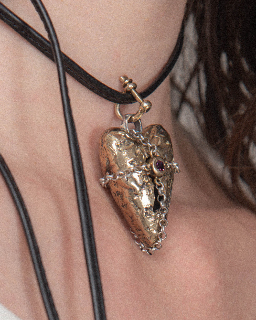 Small bronze shackle clasp used to hook a black leather choker with a heart pendant.