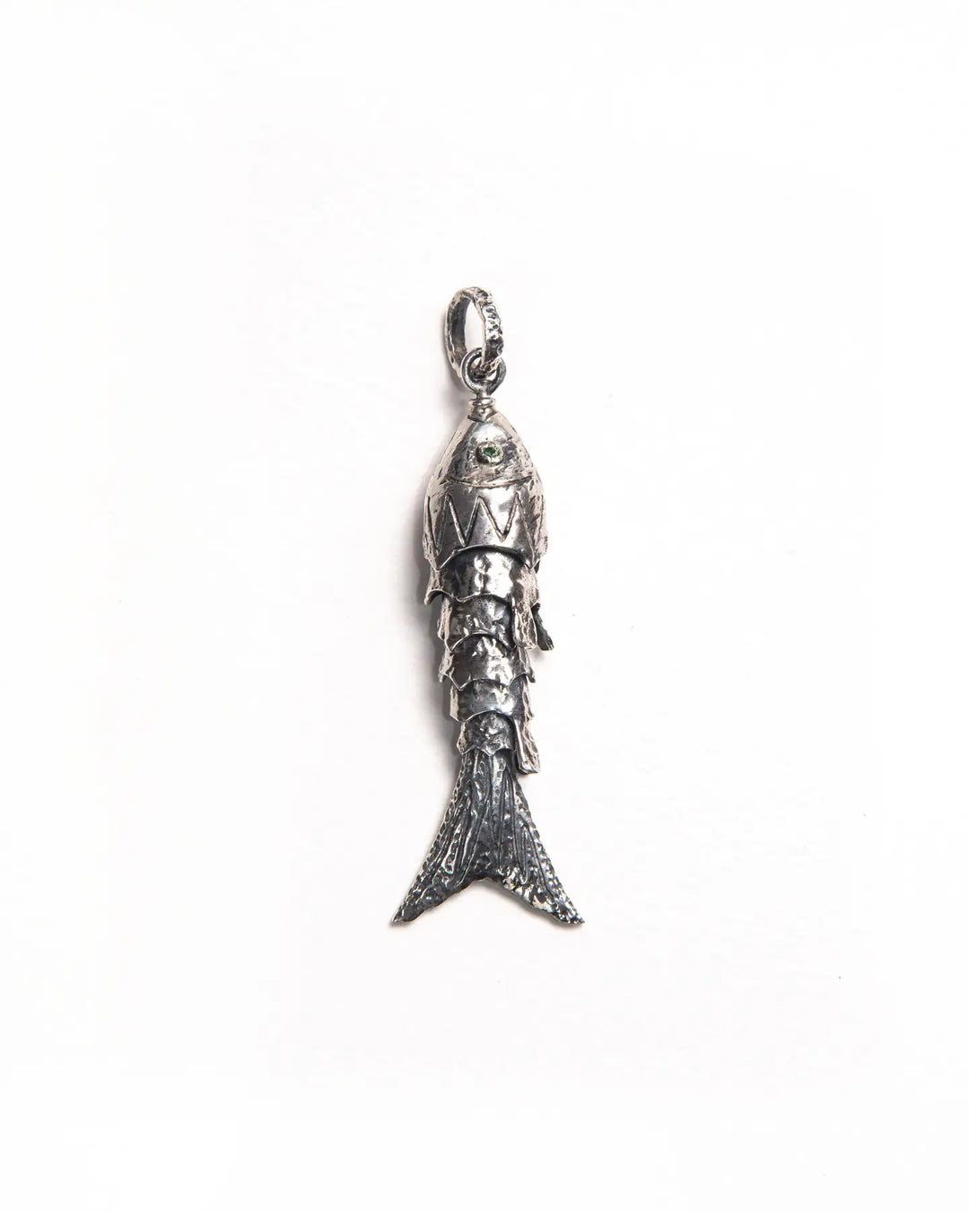 Silver maritime-inspired pendant with textured scales, peridot gemstone eyes, and a movable silhouette, designed to adorn a necklace or earring.