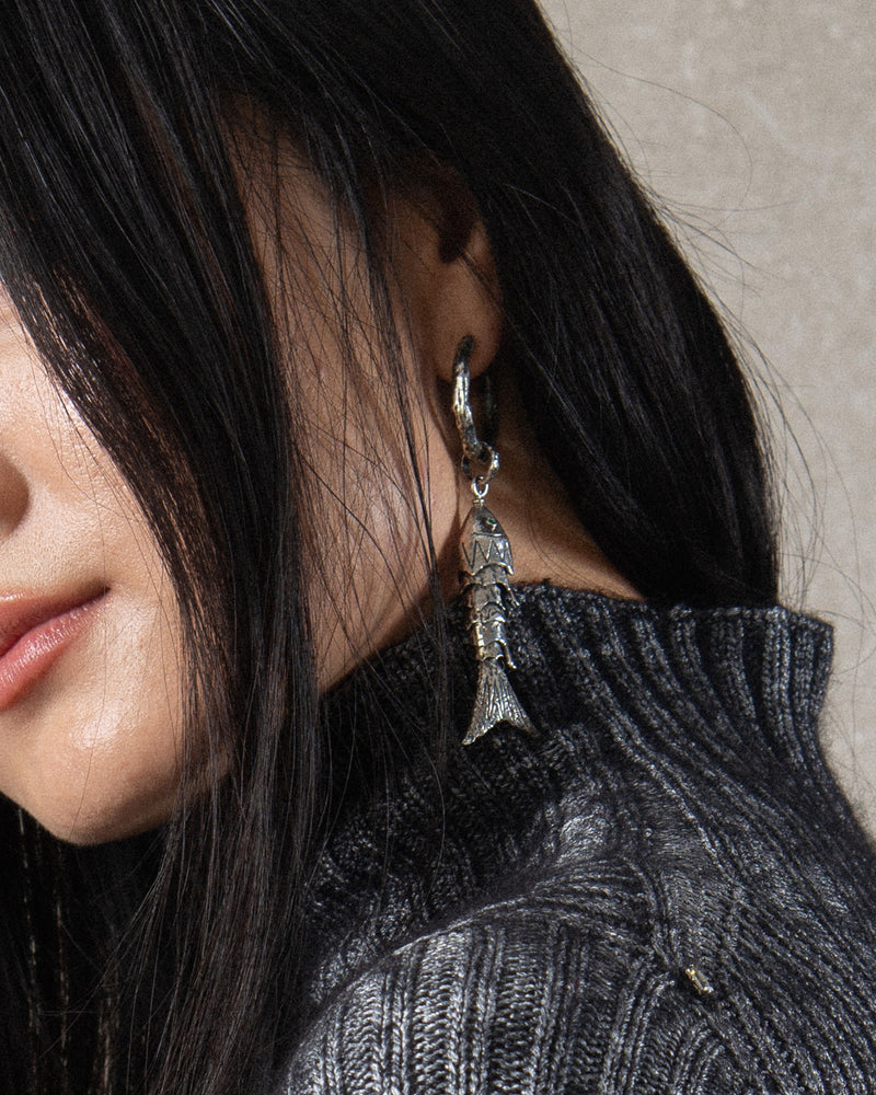 Close-up of the silver sea animal with textured scales and peridot gemstone eyes, showcasing its detailed craftsmanship and the movable silhouette as it adorns a hoop earring.