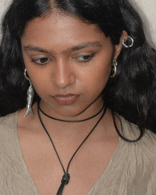 The silver fish charm with textured scales and peridot gemstone eyes is attached to a hoop earring, showcasing its detailed design and craftsmanship.