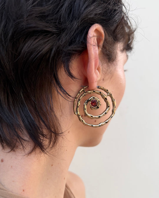 Close-up of a woman wearing a spiral earring with a red gemstone