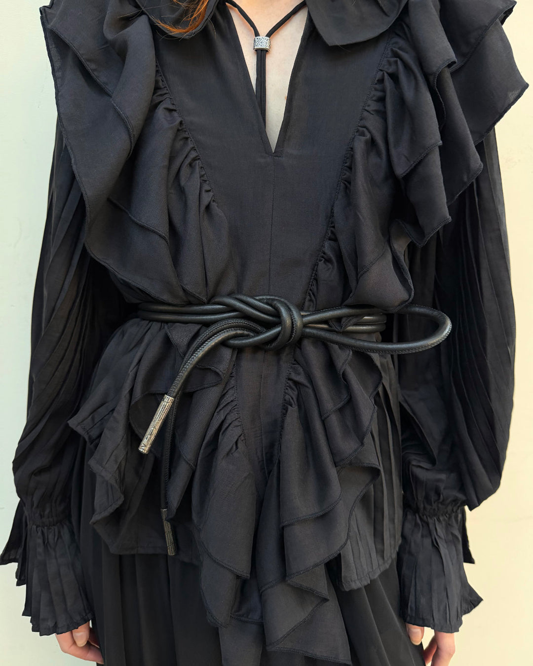 A close-up of a person wearing a black ruffled long-sleeve top or dress with a tied belt creating a beautiful chunky knot at the waist